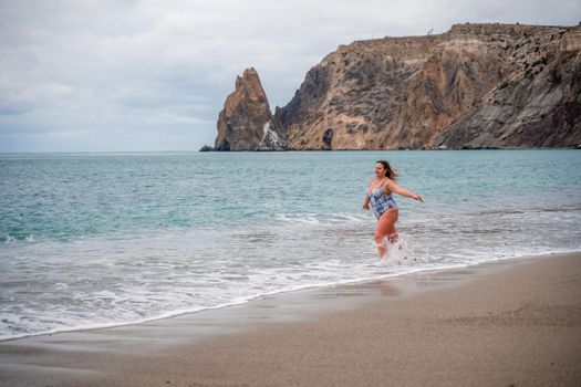 A plump woman in a bathing suit enters the water during the surf. Alone on the beach, Gray sky in the clouds, swimming in winter
