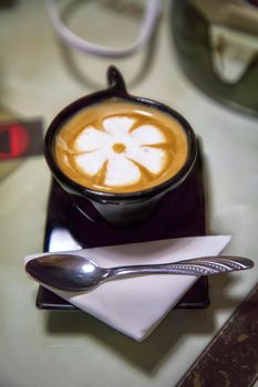 Top view of hot coffee cappuccino latte barista in a white ceramic cup with a spoon on the table.