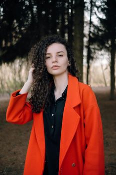 portrait of curly brunette woman in red coat in the park