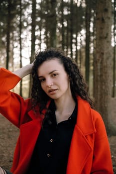 portrait of curly brunette woman in red coat in the park