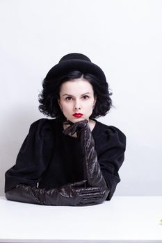 a woman with red lips, curly hair in a black hat and gloves sits at a table. High quality photo