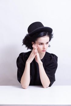 A woman in a hat sits at a table, white background. High quality photo