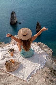 Street photo of a beautiful woman with dark hair in a mint dress and hat having a picnic on a hill overlooking the sea