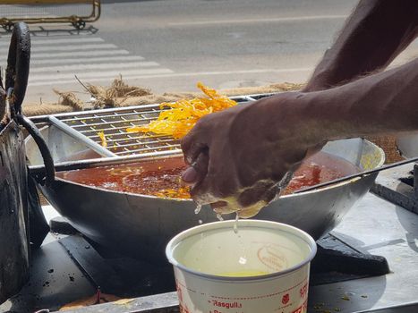 close up of shop cook deep frying many jalebi in boiling oil allowing it to rest on wire mesh making streetfood snack that is popular throughout rajasthan jaipur India for it's sweet flavor and pairing with milk
