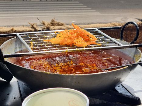 close up of shop cook deep frying many jalebi in boiling oil allowing it to rest on wire mesh making streetfood snack that is popular throughout rajasthan jaipur India for it's sweet flavor and pairing with milk