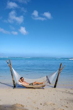 tropical beach with hammock in the ocean, white sandy beach with hammock Le Morne beach Mauritius. young men in hammock