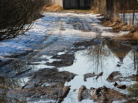 Bad country road with a rut in the spring. Difficult to pass road with snow and puddle.