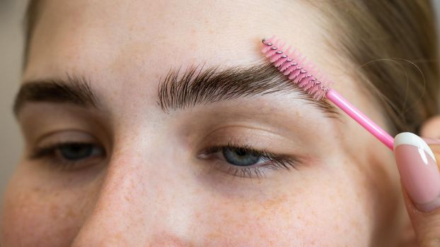 The master combs the eyebrows of the client after lamination of the eyebrows