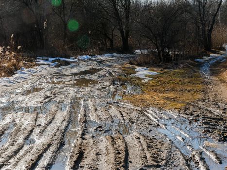 Bad dirty country road after rain. puddles and car ruts. Abandoned spring road with traces of vehicles