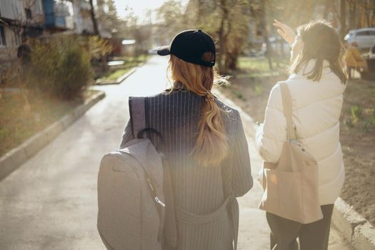 Back view portrait of two women walking and talking in a park asunny day