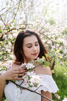 Spring concept. Nature. Young caucasian woman in white summer dress enjoying the flowering of an apple trees, walking in spring apple gardens