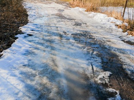 Abandoned forest road with melting snow. Dirty snowy spring road in sunny weather.