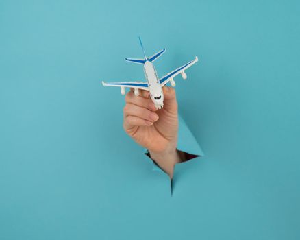 A female hand sticking out of a hole from a blue background holds a model of an airplane