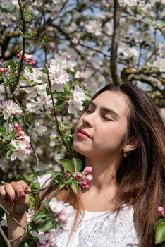 Spring concept. Nature. Young caucasian woman in white summer dress enjoying the flowering of an apple trees, walking in spring apple gardens