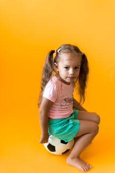 Authentic cute smiling preschool little girl with classic black and white soccer ball look at camera on yellow background. child play football in t-shirt and shorts. Sport, championship, team concept.