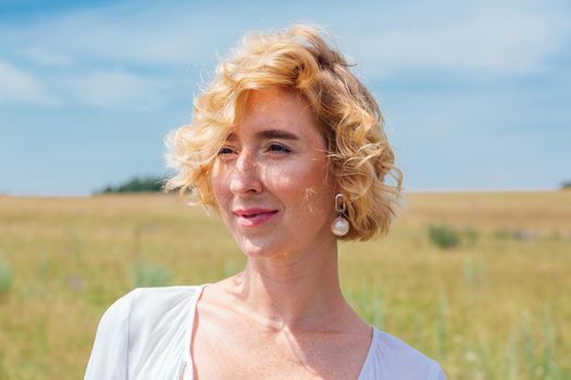 Beautiful blonde woman with short curly hair outdoors. Romantic model in summer white dress.