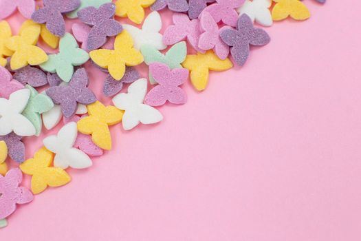 Colorful butterflies, a popular sugar confectionery topping, lie on a pink background diagonally in the left corner. Close-up. Top view. Copy space