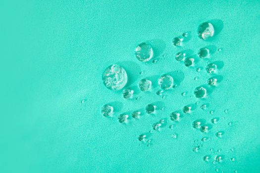 Top view of small transparent round drops of water with different shapes placed on bright green background in light studio