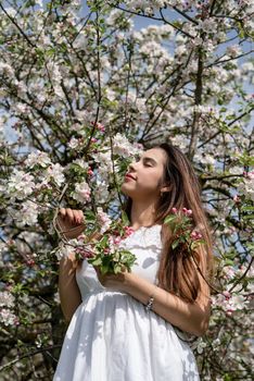 Spring concept. Nature. Young caucasian woman in white summer dress enjoying the flowering of an apple trees, walking in spring apple gardens