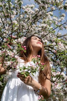 Spring concept. Nature.Young caucasian woman in white summer dress enjoying the flowering of an apple trees, walking in spring apple gardens