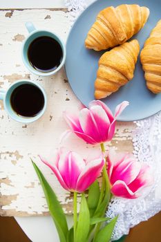 coffee, croissants and three beautiful pink tulips on old white table.