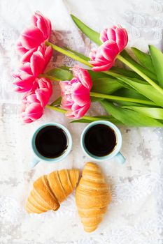 nice cup of coffee, croissants and pink tulips on old white table, close-up.