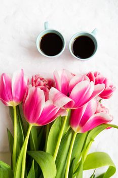 two cups of coffee and a bouquet of pink tulips.