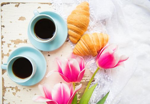 nice cup of coffee, croissants and pink tulips on old white table.