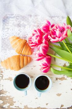 nice cup of coffee, croissants and pink tulips on old white table, close-up. valentine card