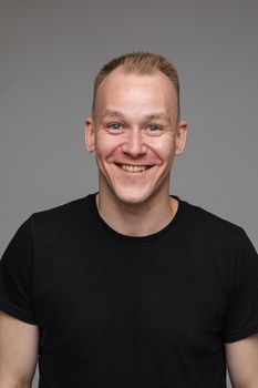 Portrait of handsome cheerful Caucasian adult man in black t-shirt smiling happily at camera. Cutout on grey background.