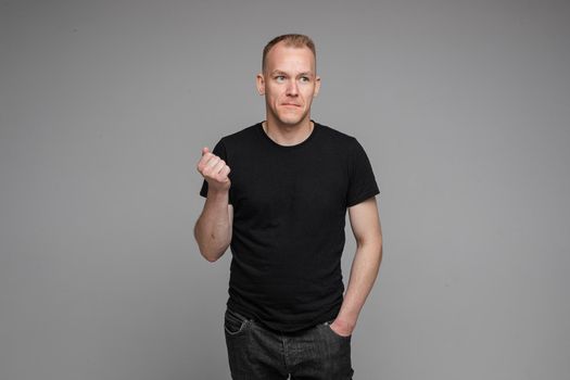 picture of caucasian man keeps his hands in the pockets of his black jeans and looks to the right isolated on grey background