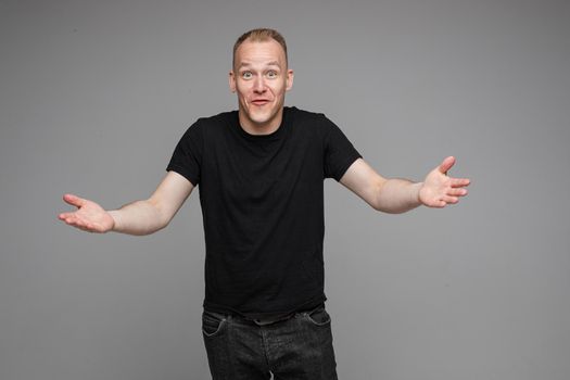 picture of caucasian man keeps his hands to the sides and looks to the camera isolated on grey background