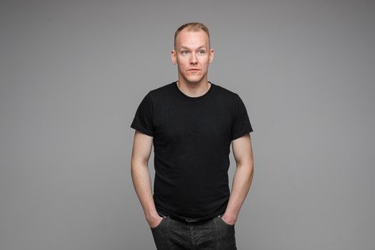 picture of caucasian man keeps his hands in the pockets of his black jeans isolated on grey background