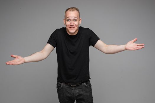 picture of caucasian man keeps his hands to the sides and looks to the camera isolated on grey background