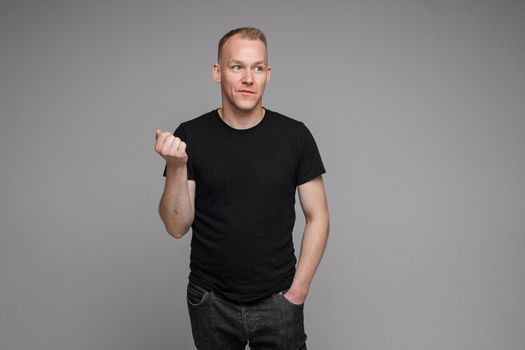 picture of caucasian man keeps his hands in the pockets of his black jeans and looks to the right isolated on grey background