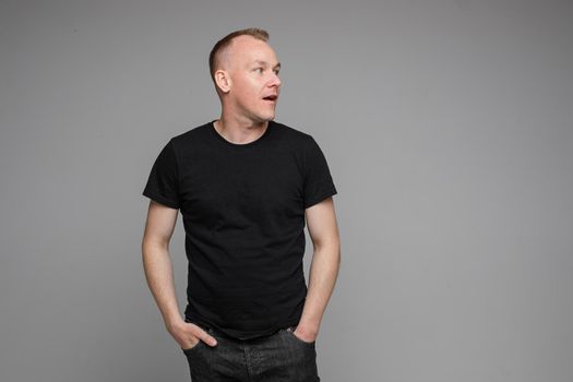 Surprised Caucasian man in black looking at camera with smile with hands on his waist.