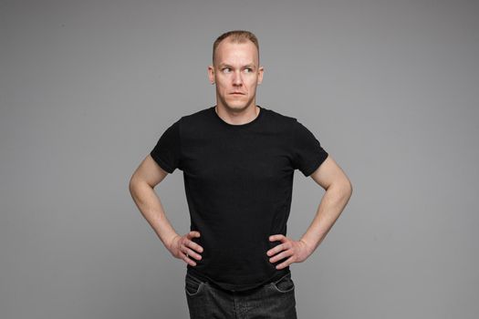 Surprised Caucasian man in black looking at camera with smile with hands on his waist.