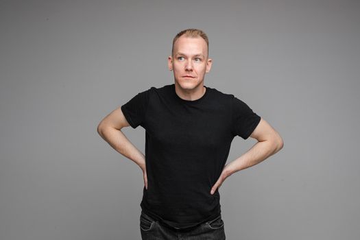 picture of handsome caucasian male keeps his hands on the belt and looks aside isolated on grey background