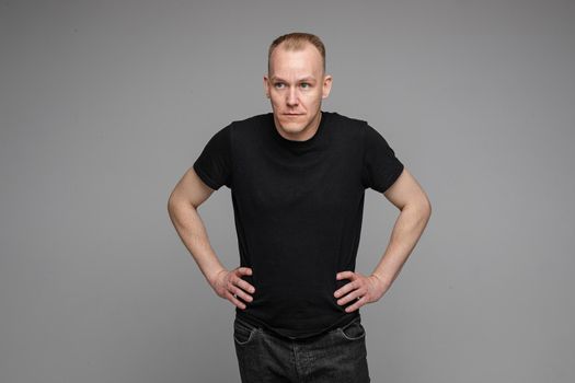 Surprised Caucasian man in black looking at camera with smile with hands on his waist.