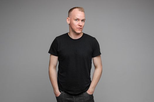 picture of handsome caucasian male keeps hands together looks with surprised sight isolated on grey background