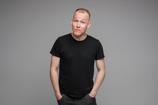 picture of handsome caucasian male keeps hands together looks with surprised sight isolated on grey background