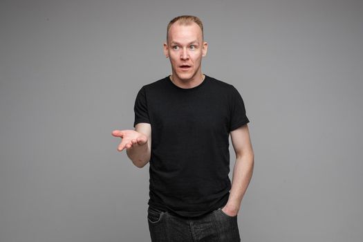 picture of handsome caucasian male keeps hands together looks with surprised sight isolated on grey background