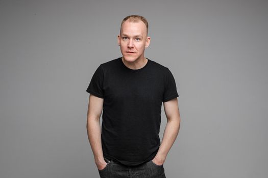 picture of handsome caucasian male keeps hands together looks with surprised sight isolated on grey background