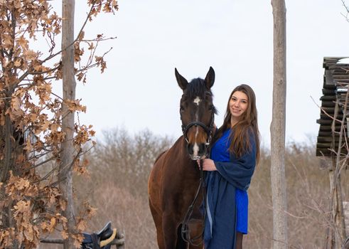 A girl in a blue dress and a horse on the background of a winter forest a