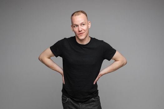 picture of handsome caucasian male keeps his hands on the belt and looks aside isolated on grey background