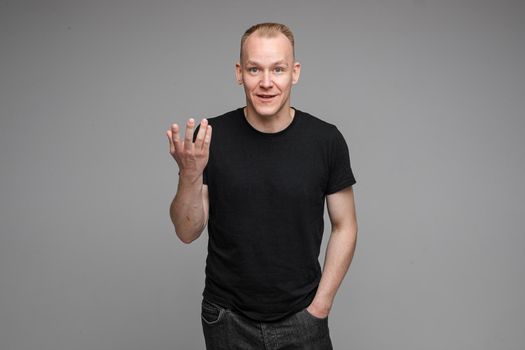 picture of handsome caucasian male keeps hands together looks with surprised sight isolated on grey background