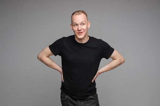 picture of handsome caucasian male keeps his hands on the belt and looks aside isolated on grey background