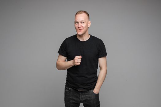Waist-up photo of playful-looking man in all black clothes holding out his fist and smiling