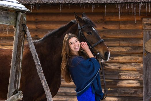 Portrait of a girl hugging a horse against the background of a wall of logs a