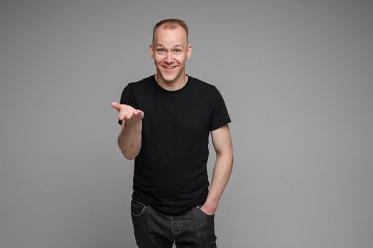picture of caucasian man keeps his hands in the pockets of his black jeans and looks to the right isolated on grey background